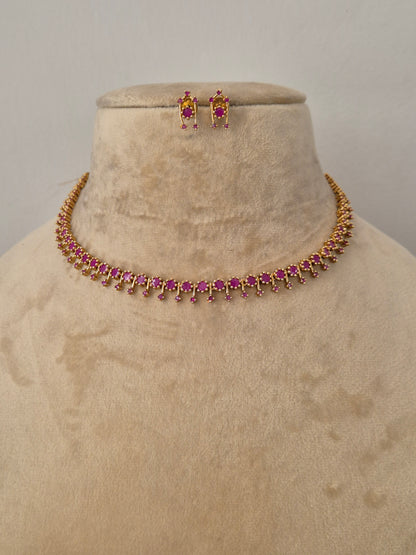 Gold-toned choker necklace and matching stud earrings with ruby-red stone embellishments by naitri.in