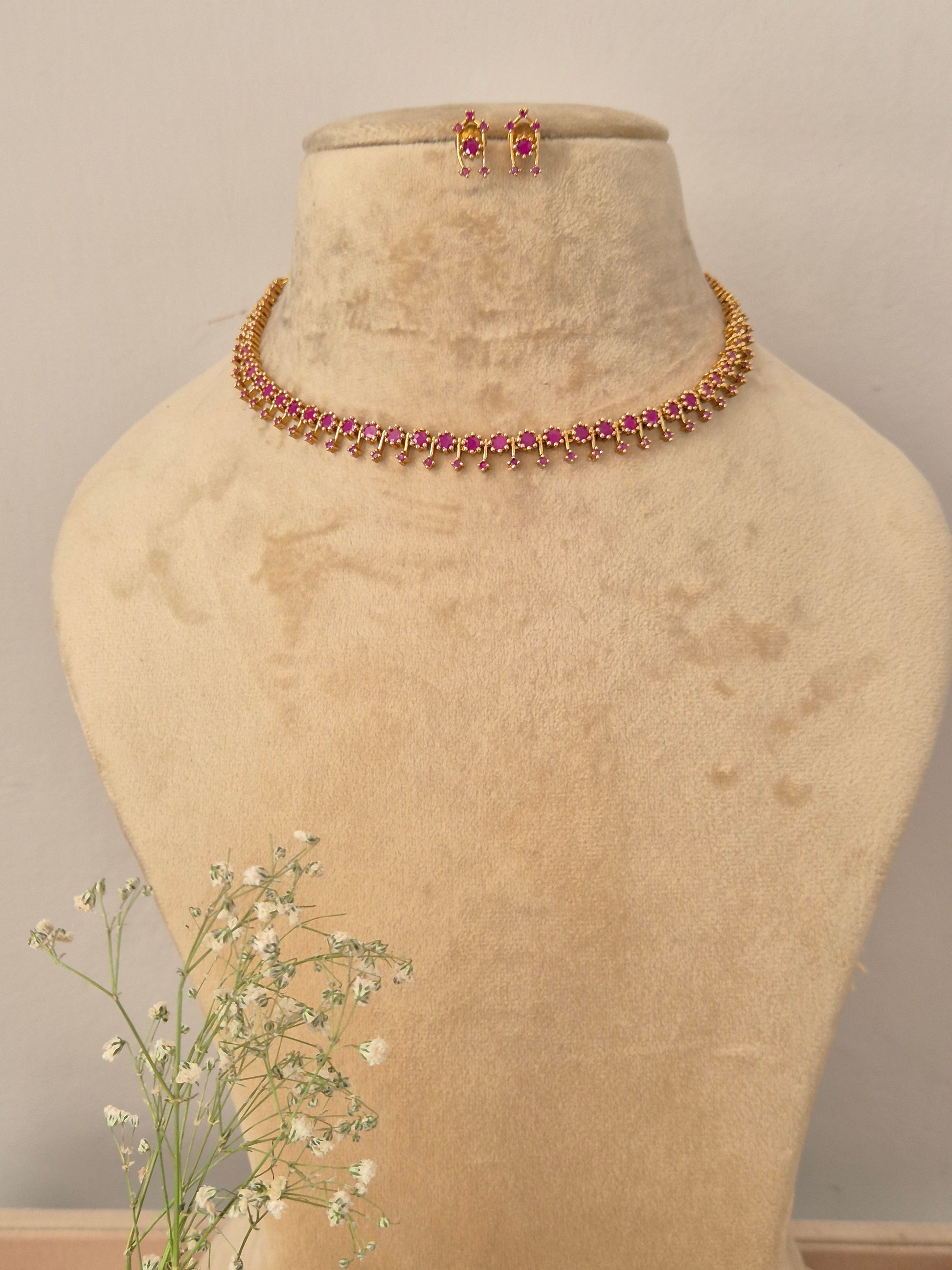 Set featuring a delicate gold-toned choker with alternating ruby-red gemstones and small golden beads, paired with matching ruby-red stone stud earrings by naitri.in