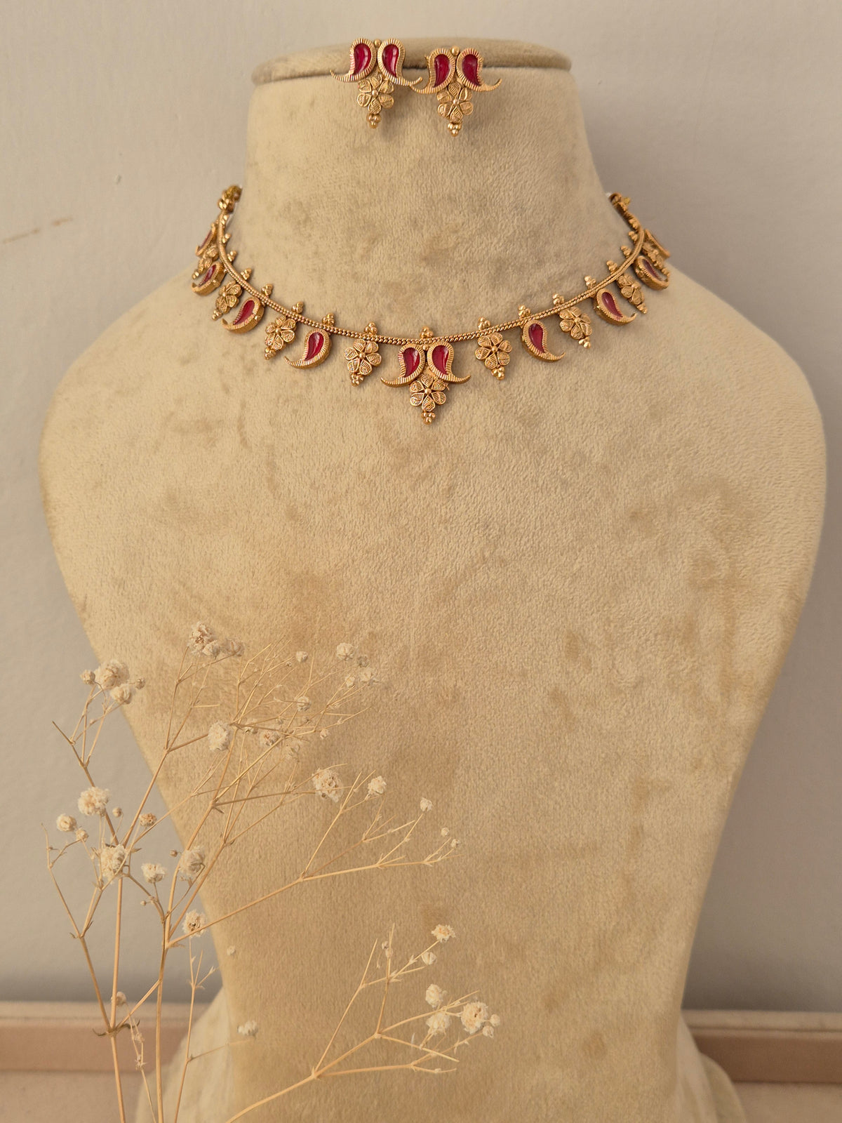 Gold-toned traditional Indian necklace and matching small dangle earrings set features intricate crescent and floral motifs inset with red-colored gemstones, accented with matching earrings by naitri.in