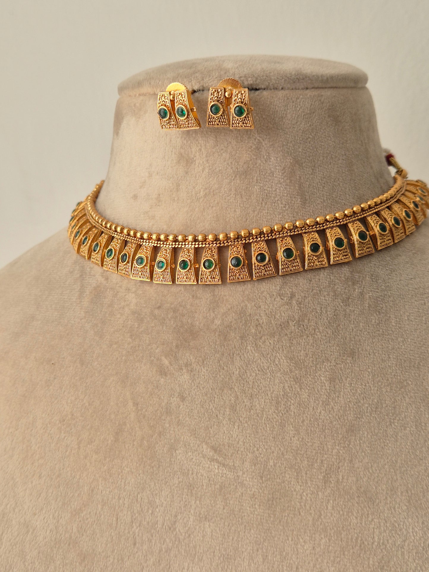 Hammered gold finish necklace set, Close-up of the filigree metalwork and green stone settings on a gold-plated brass choker by naitri.in