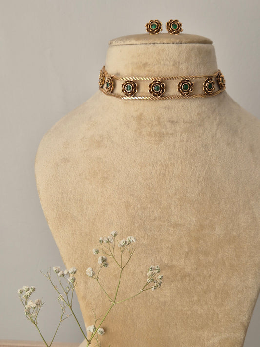 A handcrafted gold-plated brass choker with circular floral motifs, featuring green stone centers and matching stud earrings by naitri.in