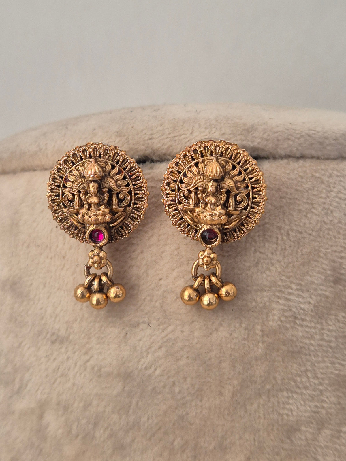 A pair of traditional Indian gold-toned earrings with detailed circular motifs depicting a deity and dangling bell charms, by naitri.in