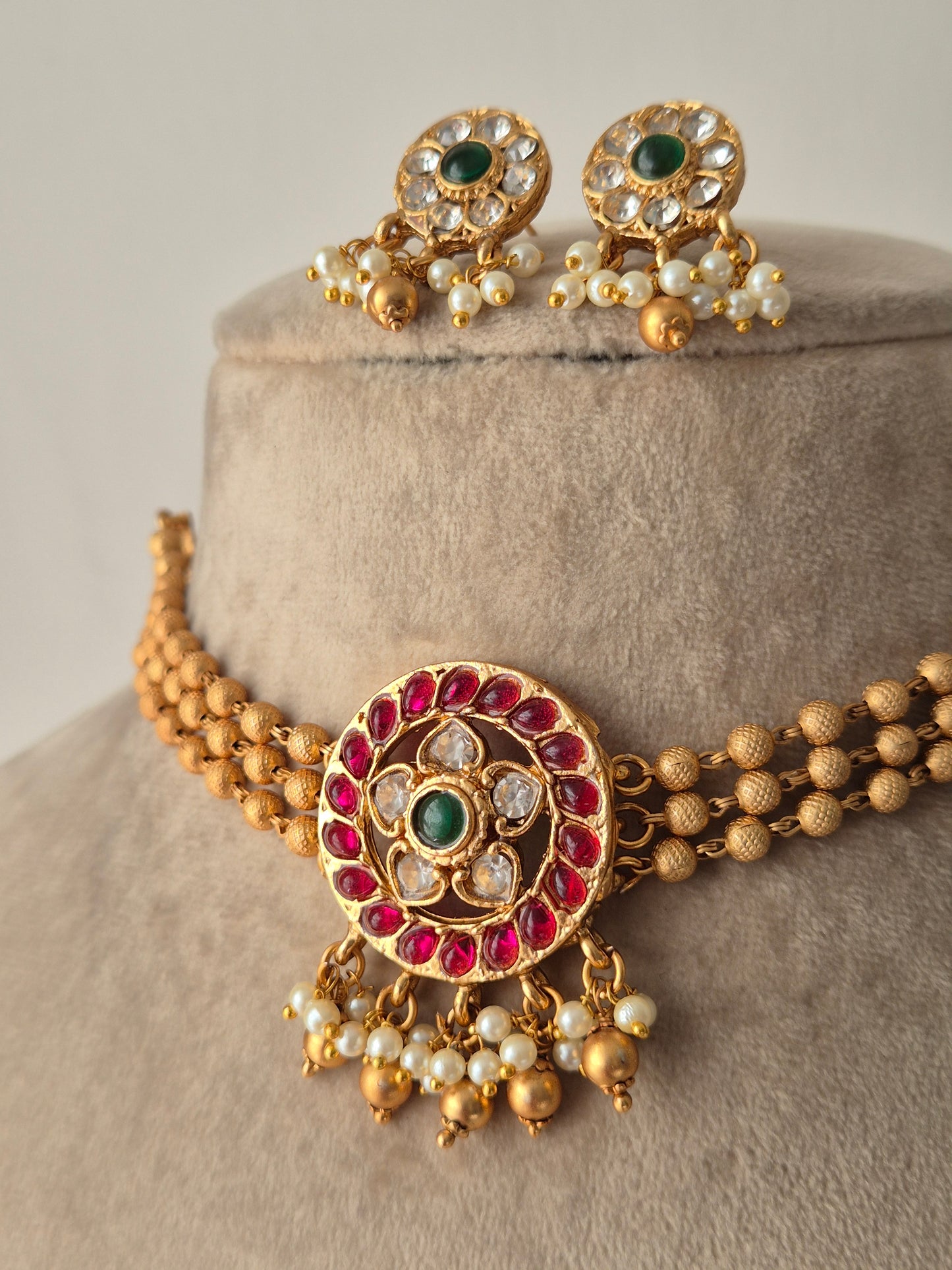 Gold bracelet with red, green and clear stones, gold beaded 3-layered chain for choker, some pearls and golden beads hanging from the pendant same designed earrings flora design choker set by naitri.in