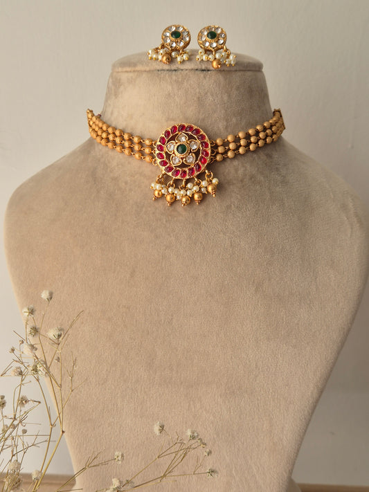 Gold bracelet with red, green and clear stones, gold beaded 3-layered chain for choker, some pearls and golden beads hanging from the pendant by naitri.in