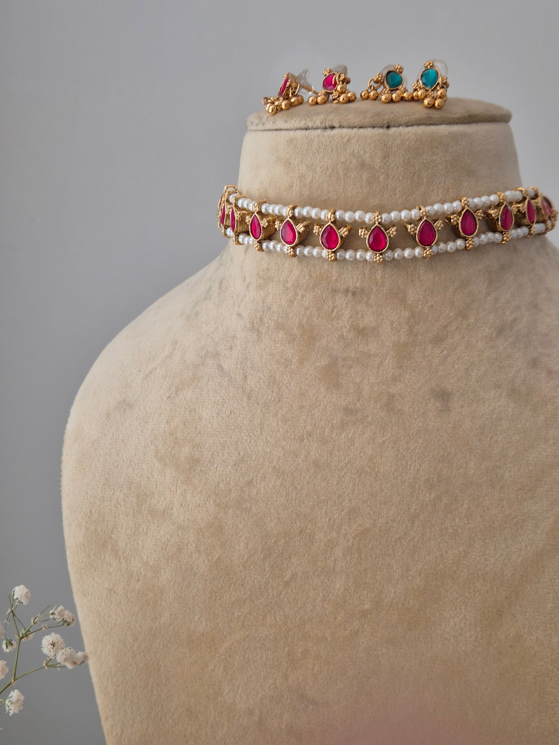 A gold-finish brass necklace with pearl strands, pink stone teardrops, and coordinating stud earrings by naitri.in