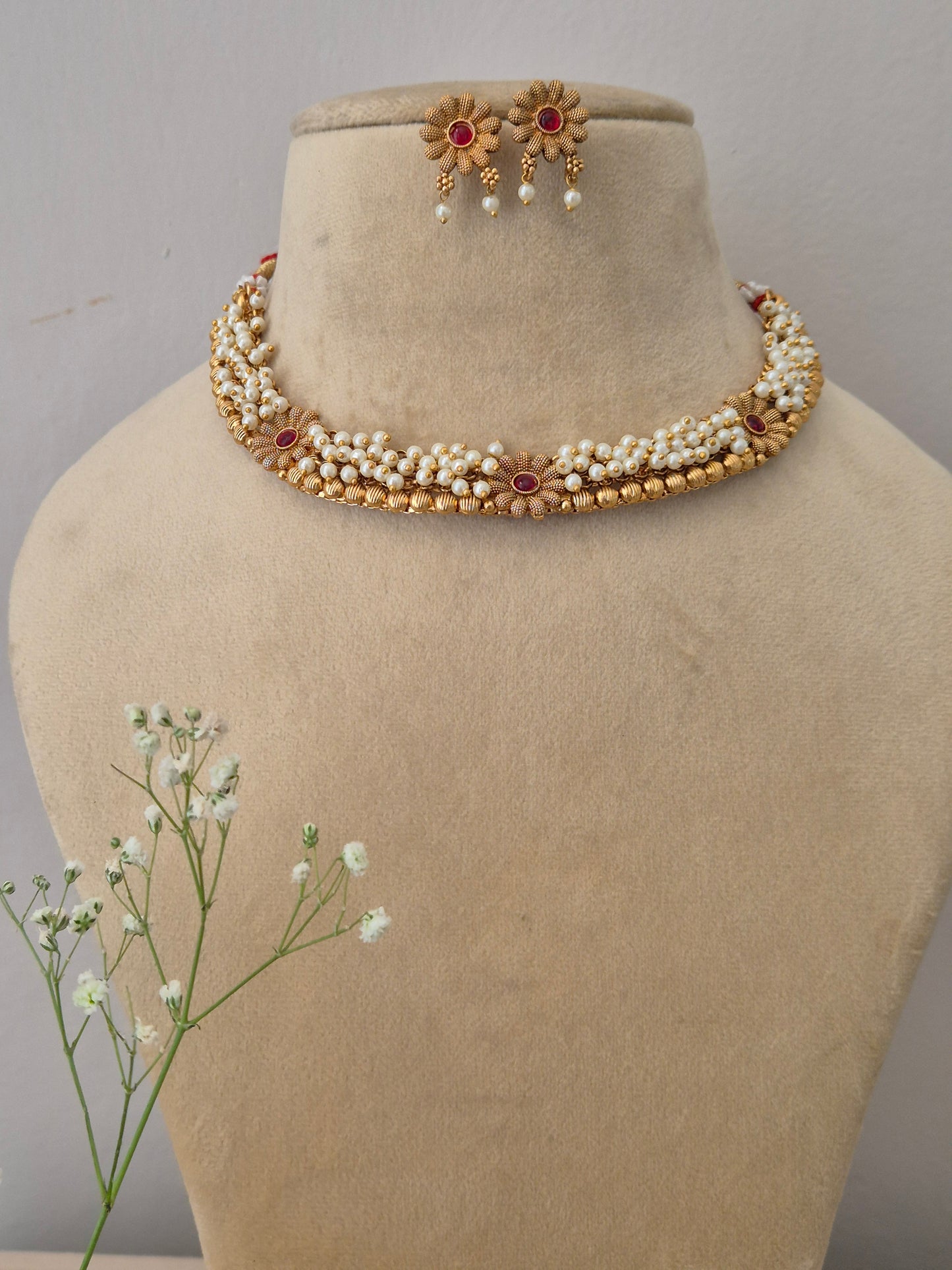 Traditional Indian gold choker necklace with pearl strands and red gemstone pendant, complete with matching stud earrings by naitri.in
