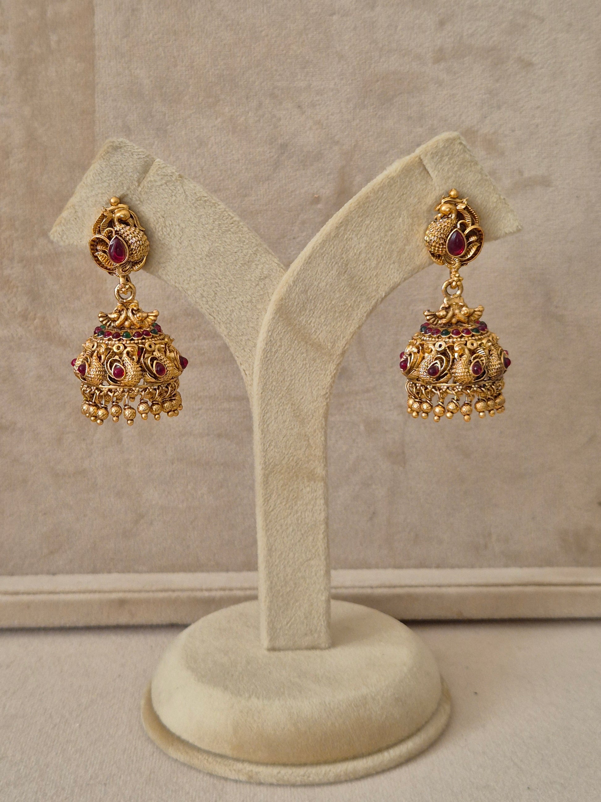 Gold temple jhumka earrings with peacock motifs and red and green stone embellishments by naitri.in