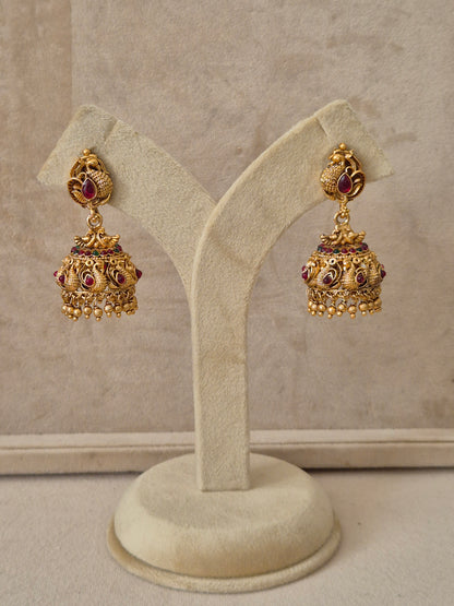Gold temple jhumka earrings with peacock motifs and red and green stone embellishments by naitri.in