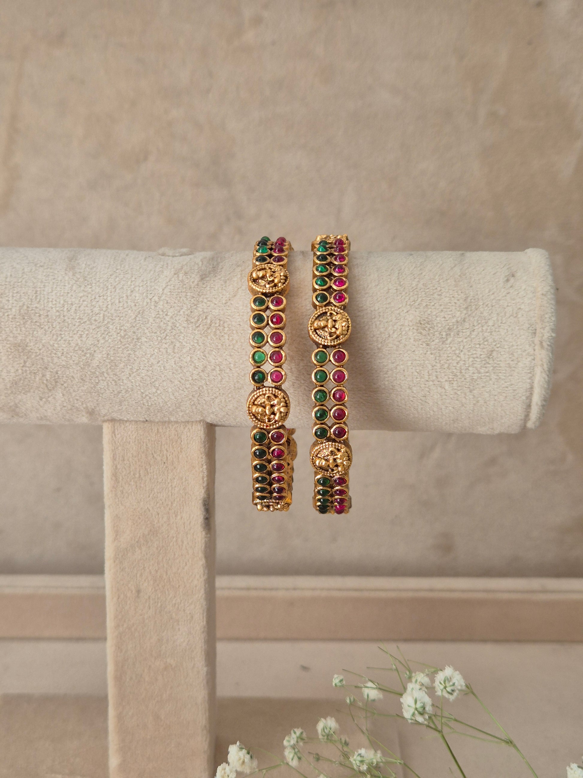 A pair of gold-plated bangles decorated with green and red stones and carved gold motifs, by naitri.in