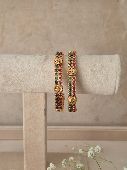 A pair of gold-plated bangles decorated with green and red stones and carved gold motifs, by naitri.in