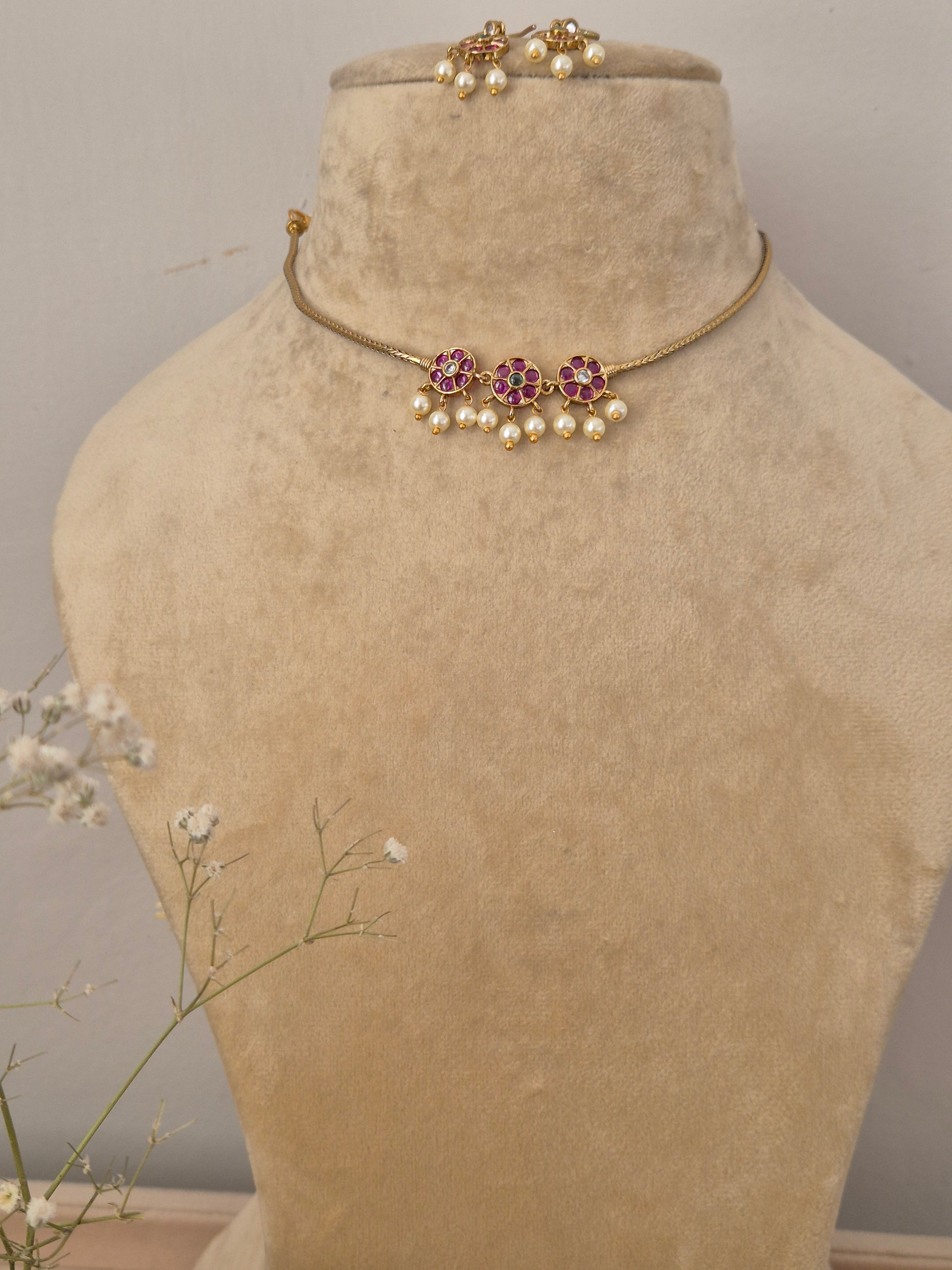 Handcrafted delicate gold-plated choker necklace featuring a central cluster of ruby-pink and emerald-green stones with dangling white seed pearls, paired with matching floral cluster drop earrings by naitri.in