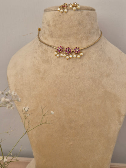 Handcrafted delicate gold-plated choker necklace featuring a central cluster of ruby-pink and emerald-green stones with dangling white seed pearls, paired with matching floral cluster drop earrings by naitri.in
