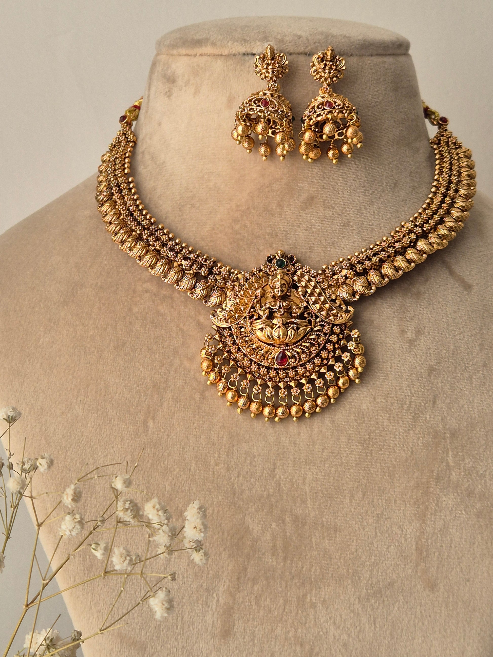 Gold necklace and earrings with red- green stones goddess motif and golden beads attached with pendant and jhumki by naitri.in