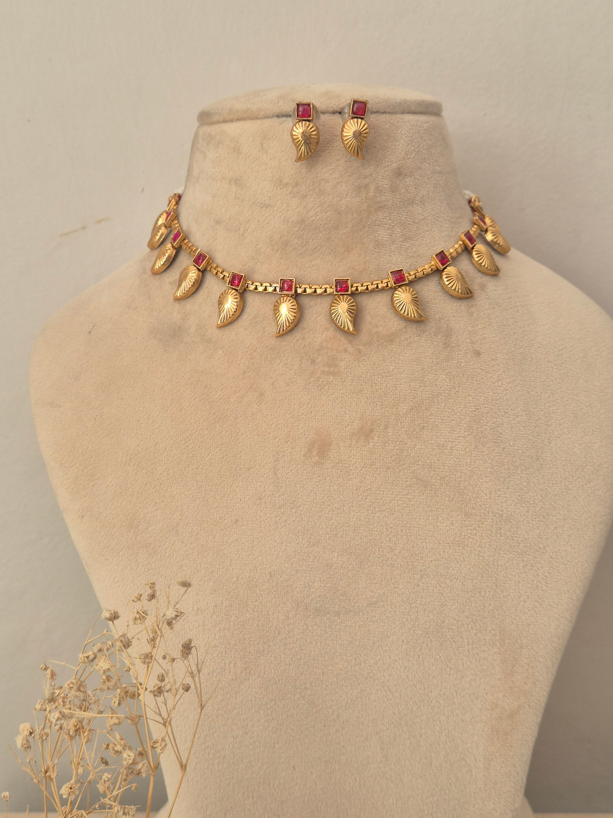 Gold choker necklace set featuring textured leaf-shaped motifs set with small red stones matching stud earrings by naitri.in