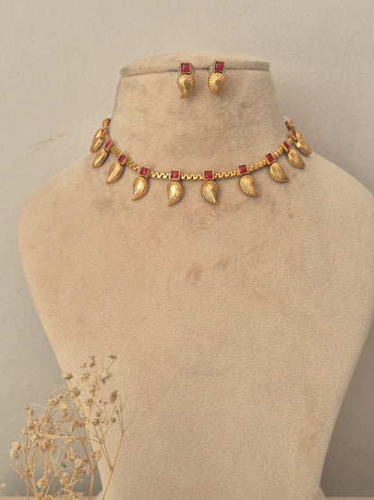 Gold choker necklace set featuring textured leaf-shaped motifs set with small red stones matching stud earrings by naitri.in