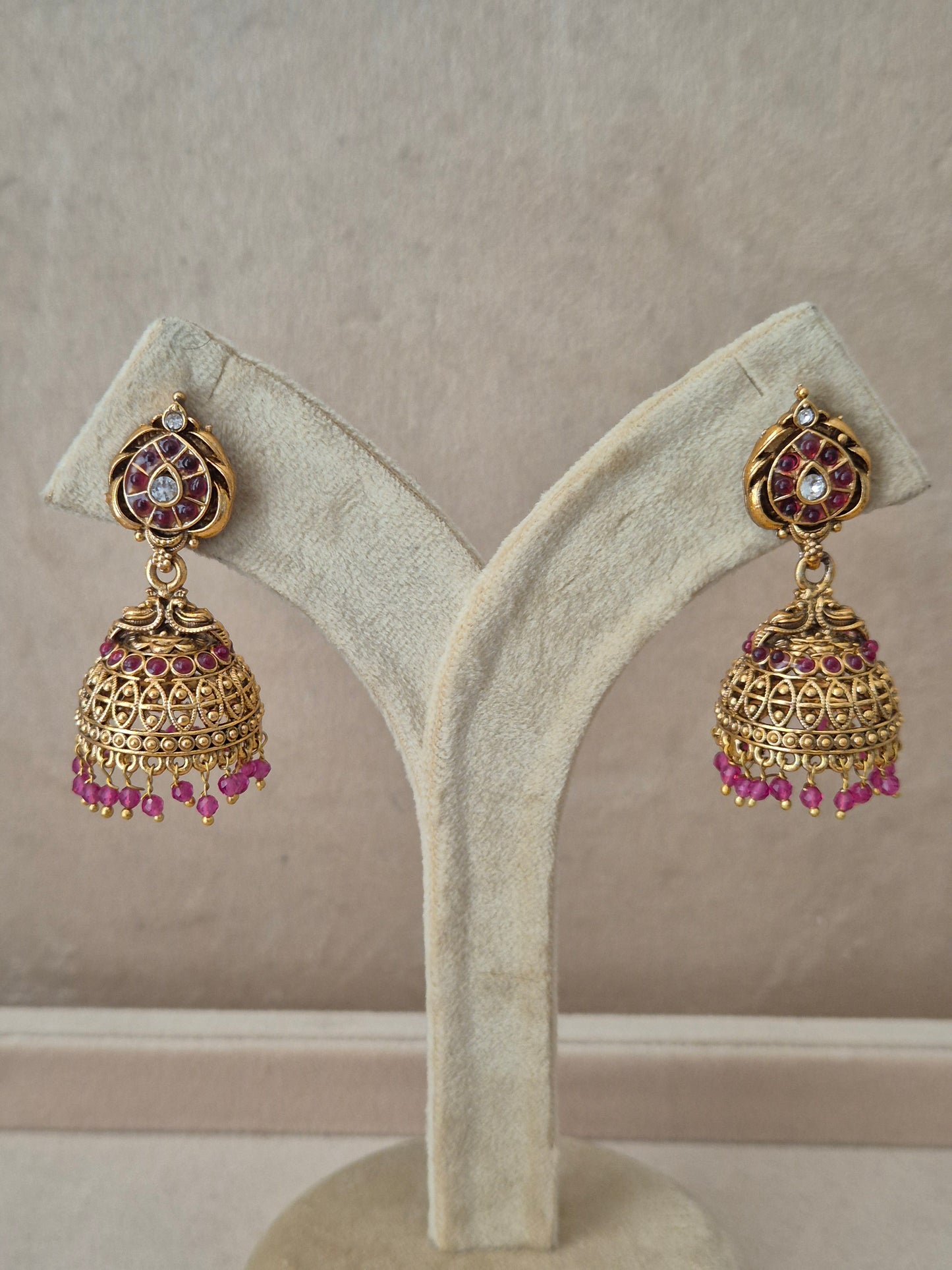 Traditional gold-toned temple design Jhumka earrings with pink stone embellishments and dangling bead fringe. by naitri.in