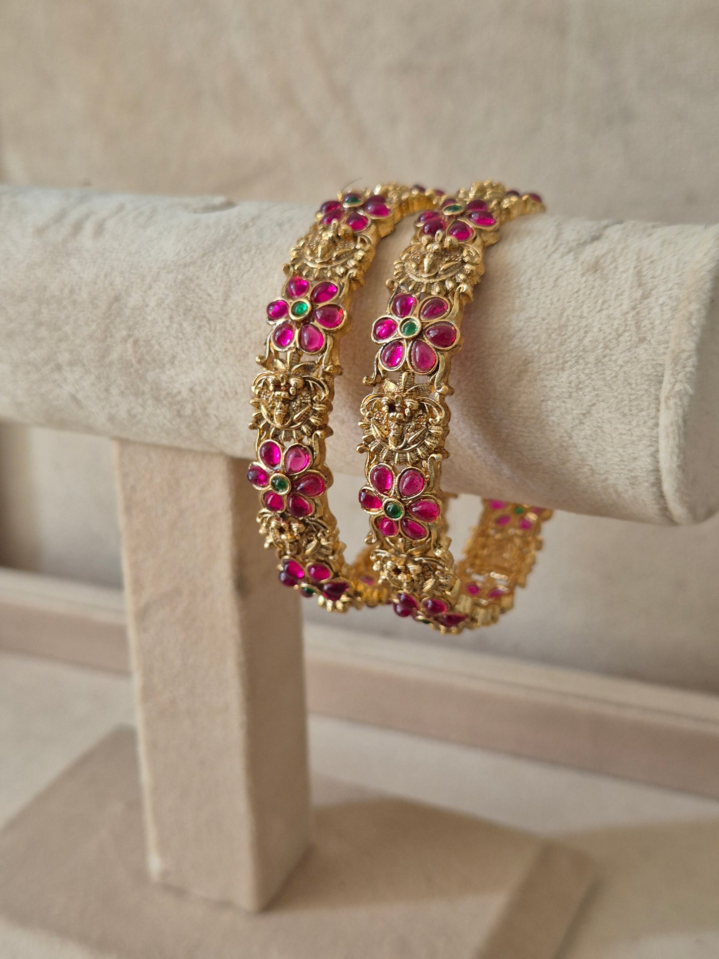 Set of two traditional gold-toned festive bangles with red and green gemstones by naitri.in