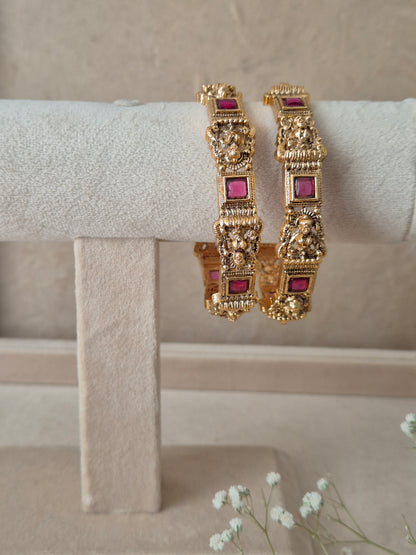 Pair of Naitri's Urmila gold bangles showcasing premium antique craftsmanship, embedded with vibrant pinkish-red gemstone accents, by naitri.in