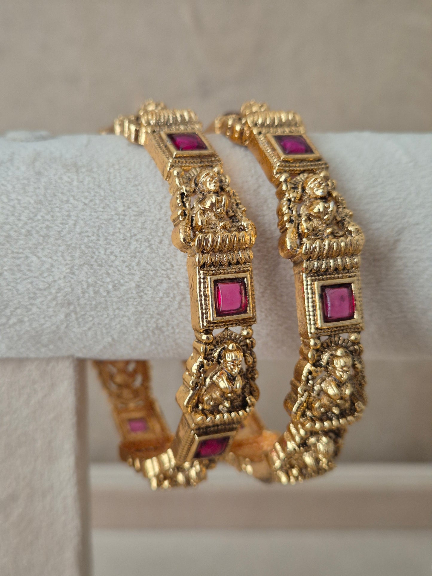 Two traditional gold-plated ethnic bangles with detailed deity engravings and inlaid square red gemstones by naitri.in