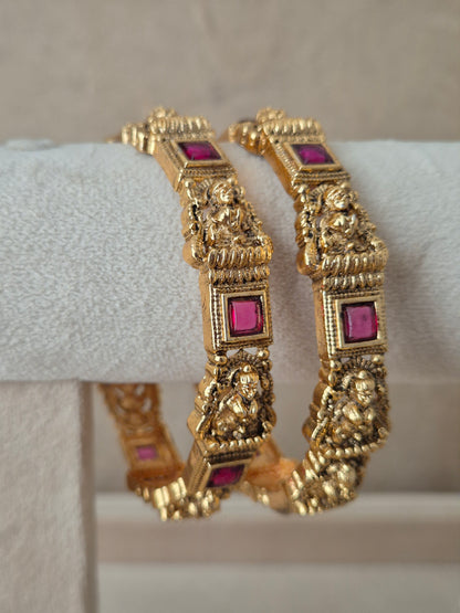 Two traditional gold-plated ethnic bangles with detailed deity engravings and inlaid square red gemstones by naitri.in
