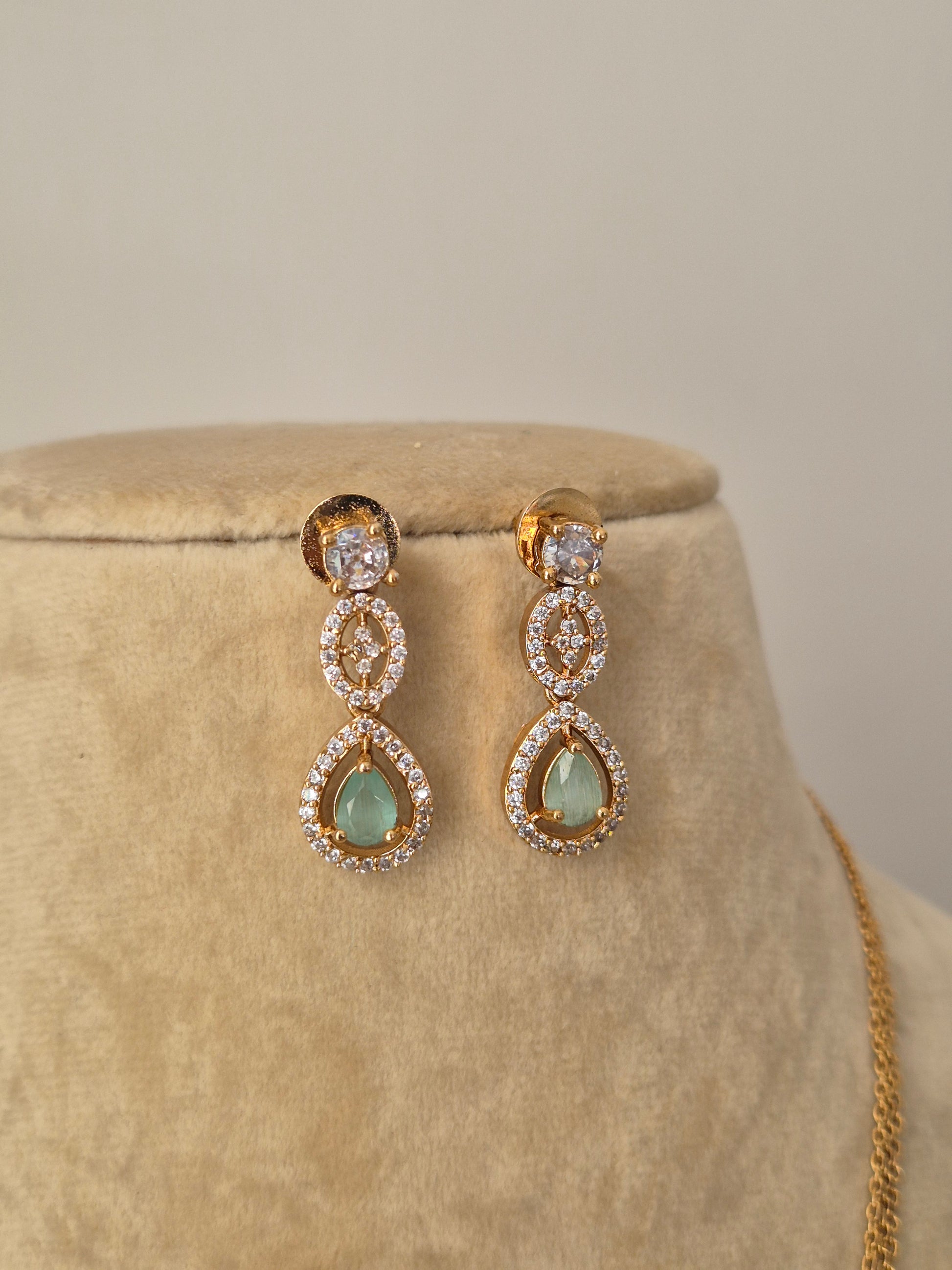 Minimalist golden necklace featuring a central cluster of green stones in a teardrop setting with matching stud earrings by naitri.in