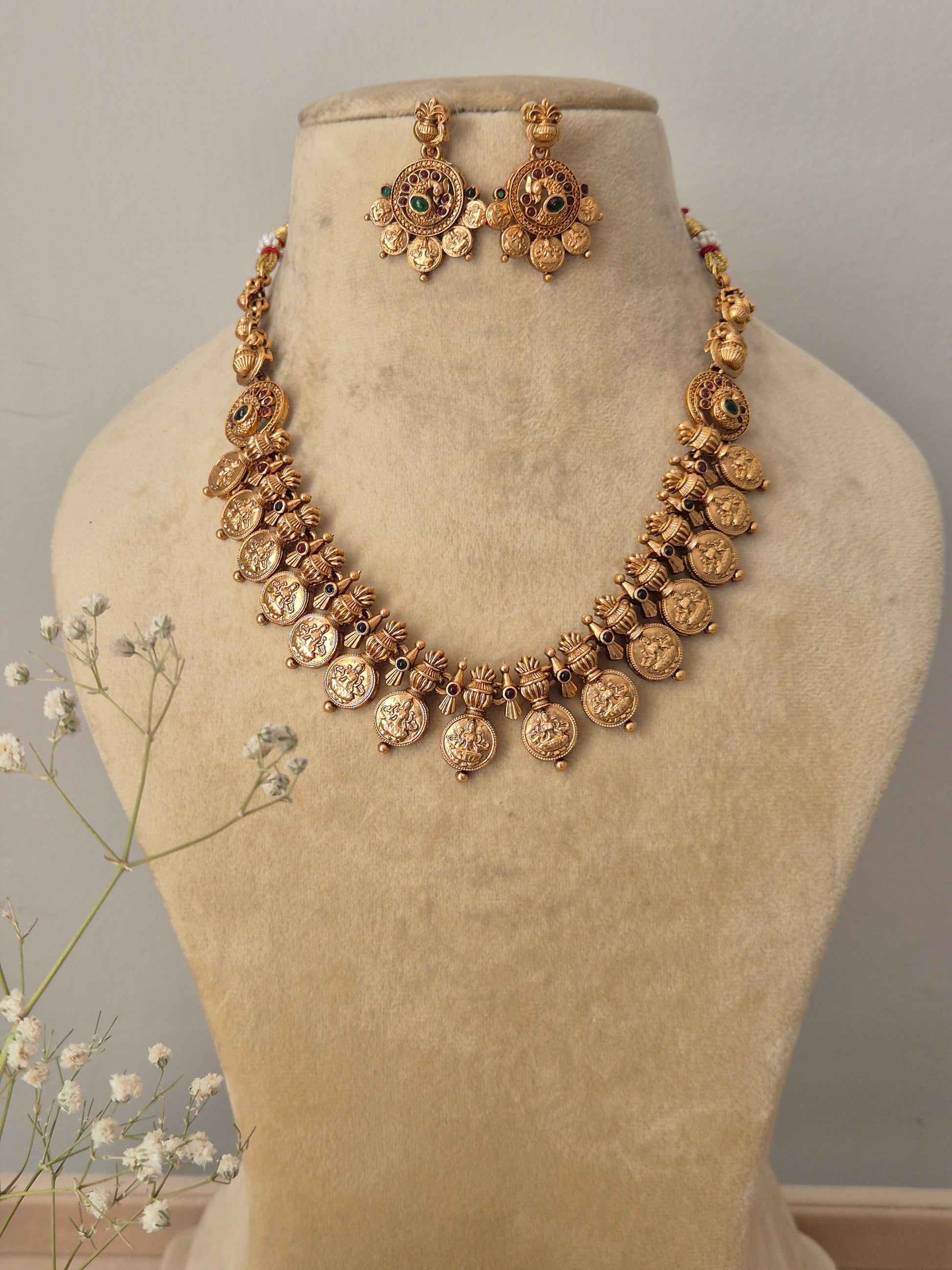 : Handcrafted gold-polished brass strand necklace featuring traditional coin charms, green and red stone accents, and matching round drop earrings by naitri.in