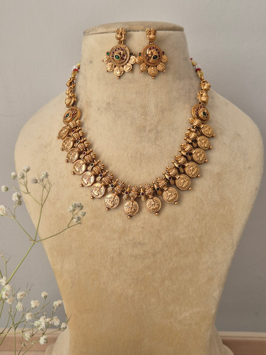 : Handcrafted gold-polished brass strand necklace featuring traditional coin charms, green and red stone accents, and matching round drop earrings by naitri.in