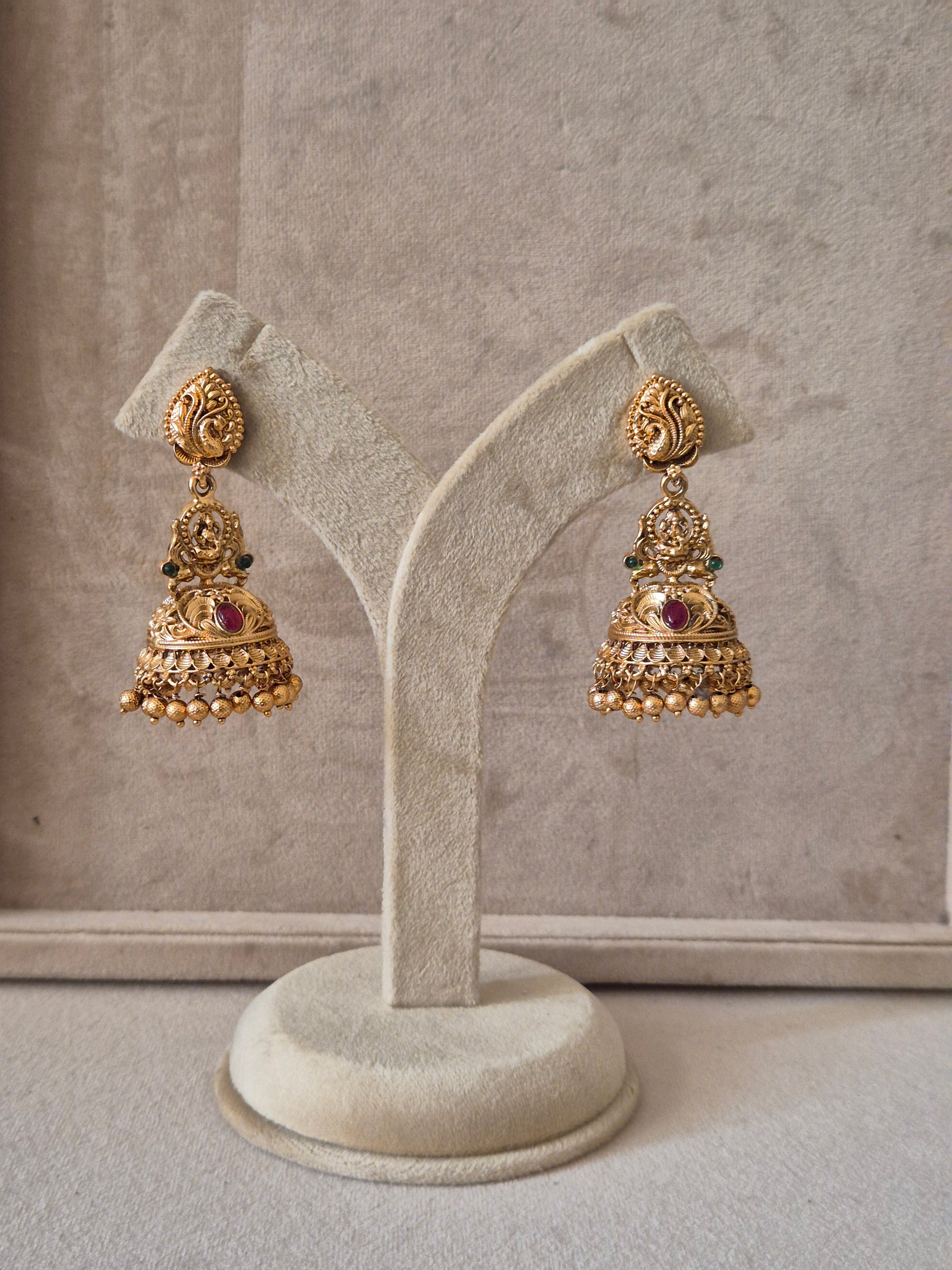 Traditional gold-toned  earrings with intricate peacock-etched studs, red and green gemstone accents, and delicate gold bead clusters  by naitri.in