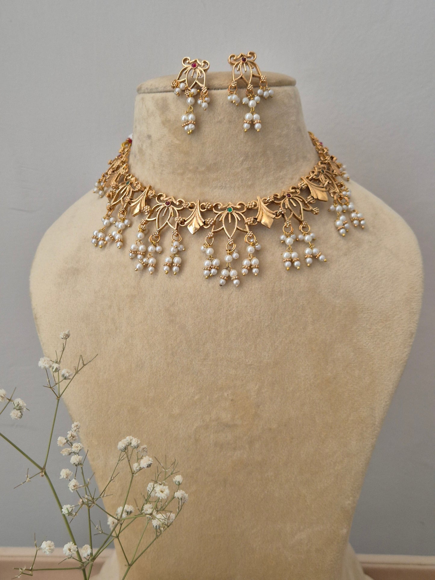 Elegant gold-plated with traditional leaf motifs and hanging pearl clusters, displayed on a beige mannequin stand with a matching pair of earrings by naitri.in