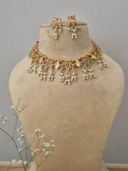 Elegant gold-plated with traditional leaf motifs and hanging pearl clusters, displayed on a beige mannequin stand with a matching pair of earrings by naitri.in