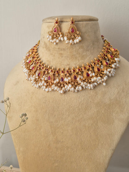 Handcrafted gold temple jewelry choker necklace and matching drop earrings with red stones and pearl cluster fringes by naitri.in