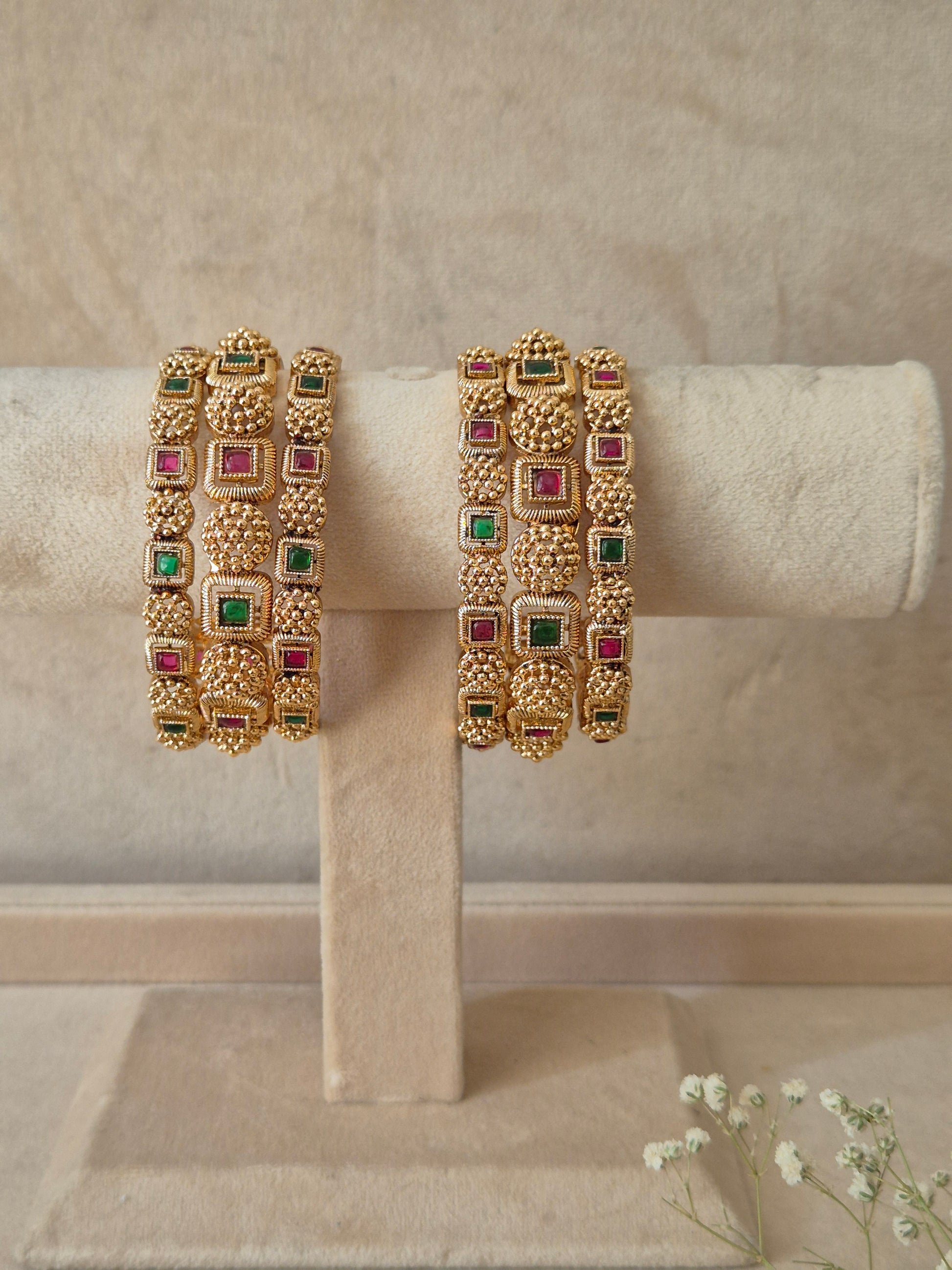 A set of six gold-plated Uttura bangles featuring intricate traditional engraving inlaid with alternating square-cut red and green gemstones,