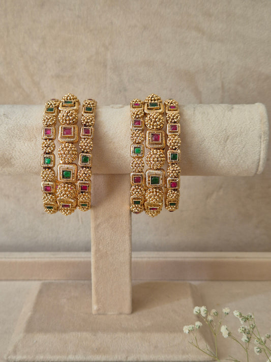 A set of six gold-plated Uttura bangles featuring intricate traditional engraving inlaid with alternating square-cut red and green gemstones,