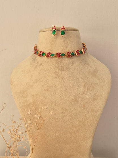 Vasundhara Necklace Set featuring a gold-toned choker with alternating green teardrop stones and pink floral motifs, accompanied by matching teardrop stud earrings by Naitri.in