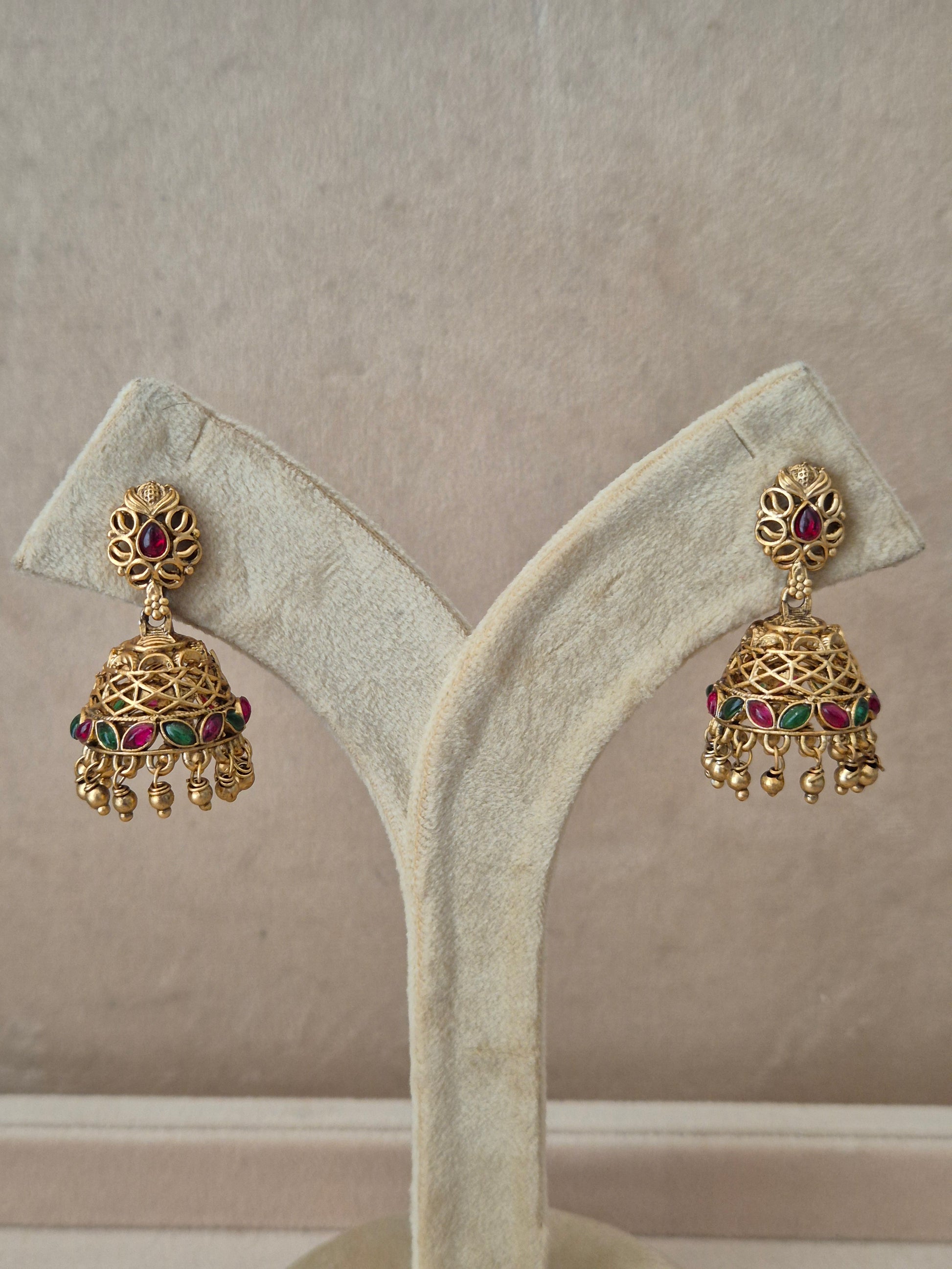 Traditional gold-toned Vedshri Jhumka earrings with red and green gemstone embellishments and dangling gold beads by naitri.in