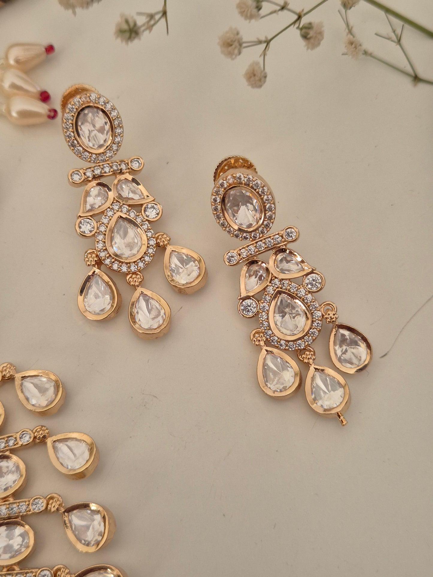 Matching Victoria American Diamond drop earrings with a floral stud and teardrop crystal, displayed alongside the coordinating stately choker necklace by naitri.in by naitri.in