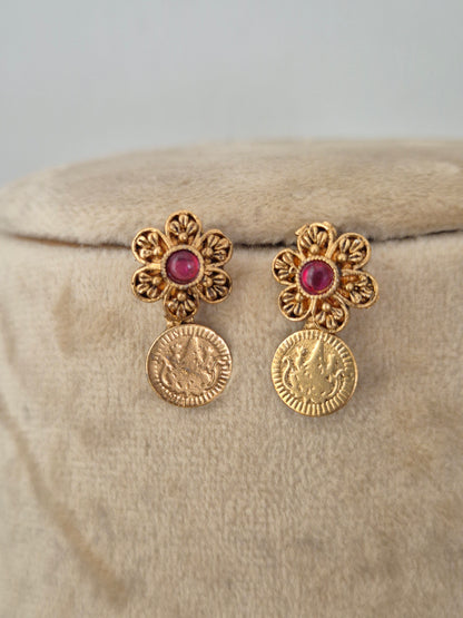 A pair of gold-toned drop earrings, each earring features an ornate flower-shaped top with a round pinkish-red center stone, connected to a dangling coin-shaped charm by naitri.in