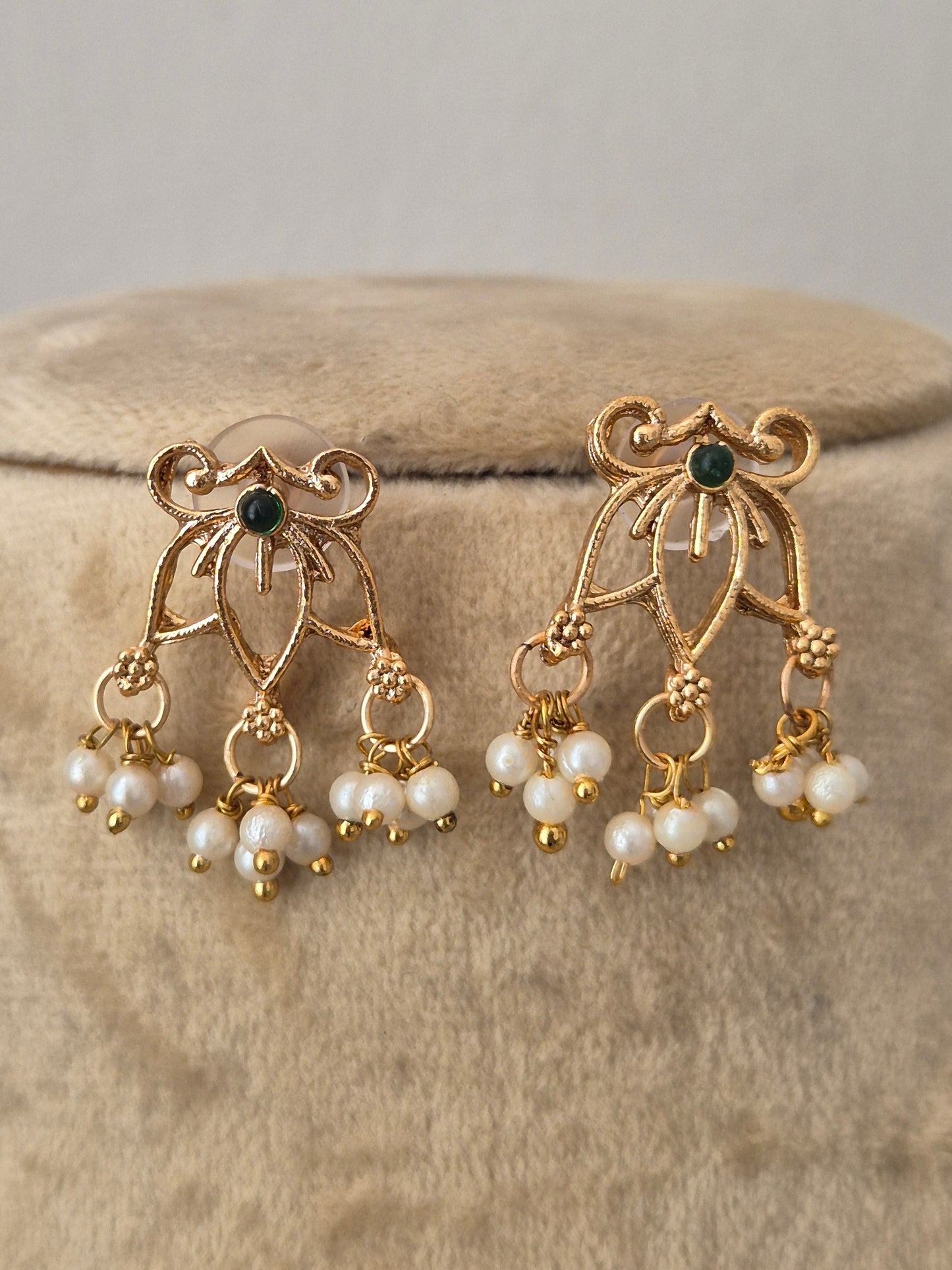 A pair of gold-toned dangle earrings with small dark green stones and clusters of white faux pearls, by naitri.in