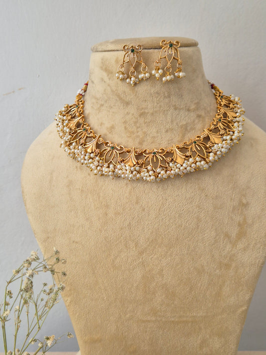 Gold-toned traditional Indian choker necklace and matching drop earrings set features intricate, textured floral and leaf motifs with a delicate fringe of hanging tiny white pearl beads, paired with matching dangle earrings by naitri.in