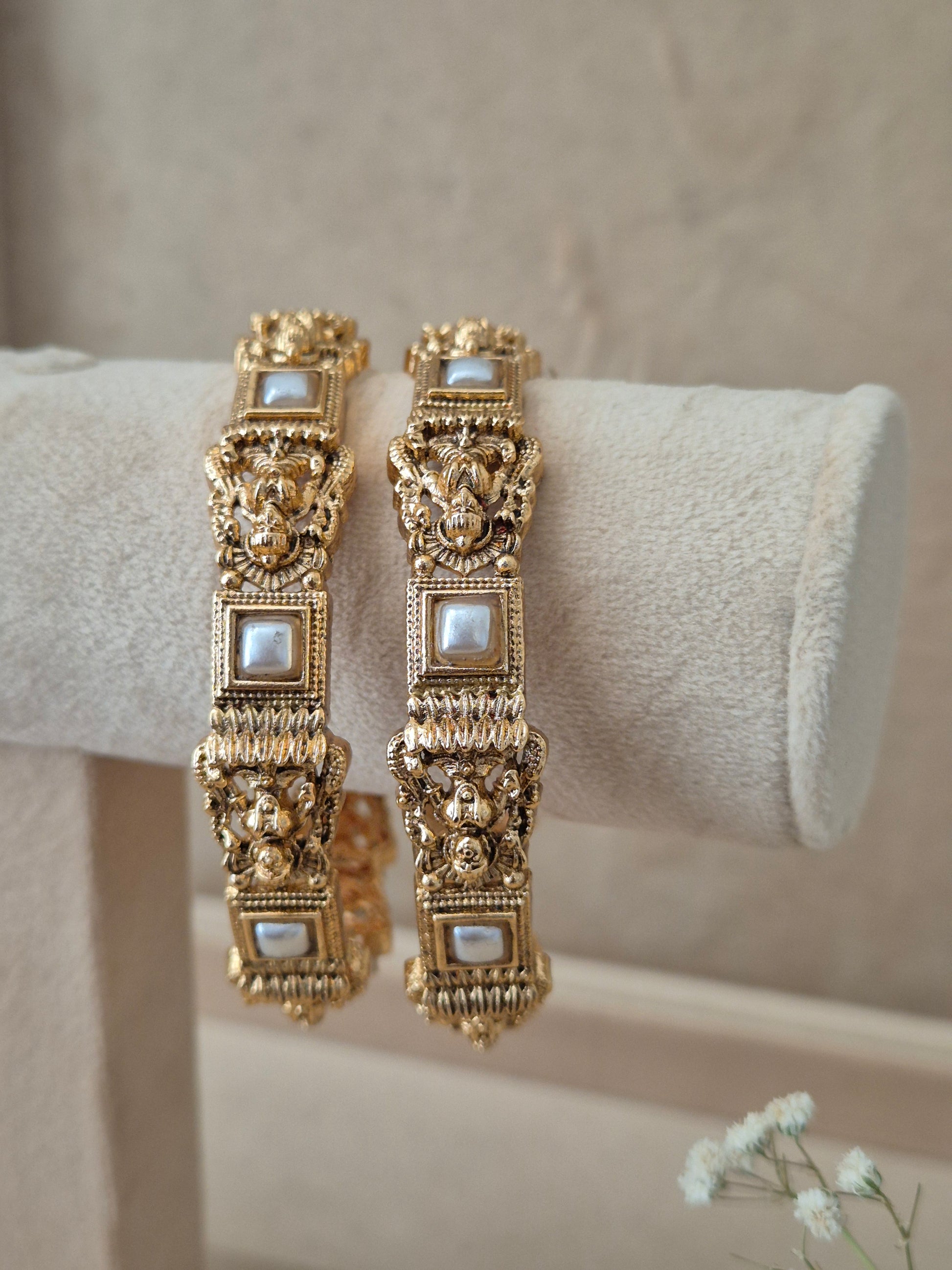Two traditional gold-plated ethnic bangles with detailed textured patterns and inlaid square white stones By naitri.in