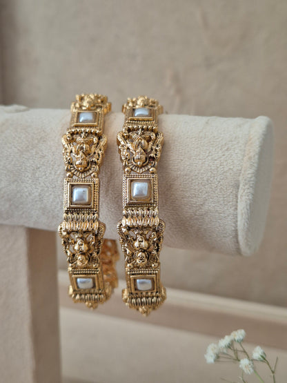 Two traditional gold-plated ethnic bangles with detailed textured patterns and inlaid square white stones By naitri.in