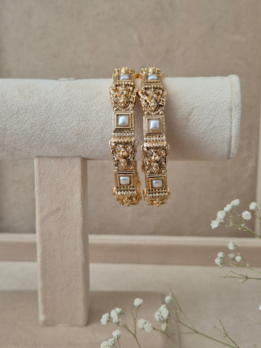 Set of 2 Visha gold bangles by Naitri featuring intricate traditional filigree engravings, accented with square-framed white pearls, by naitri.in