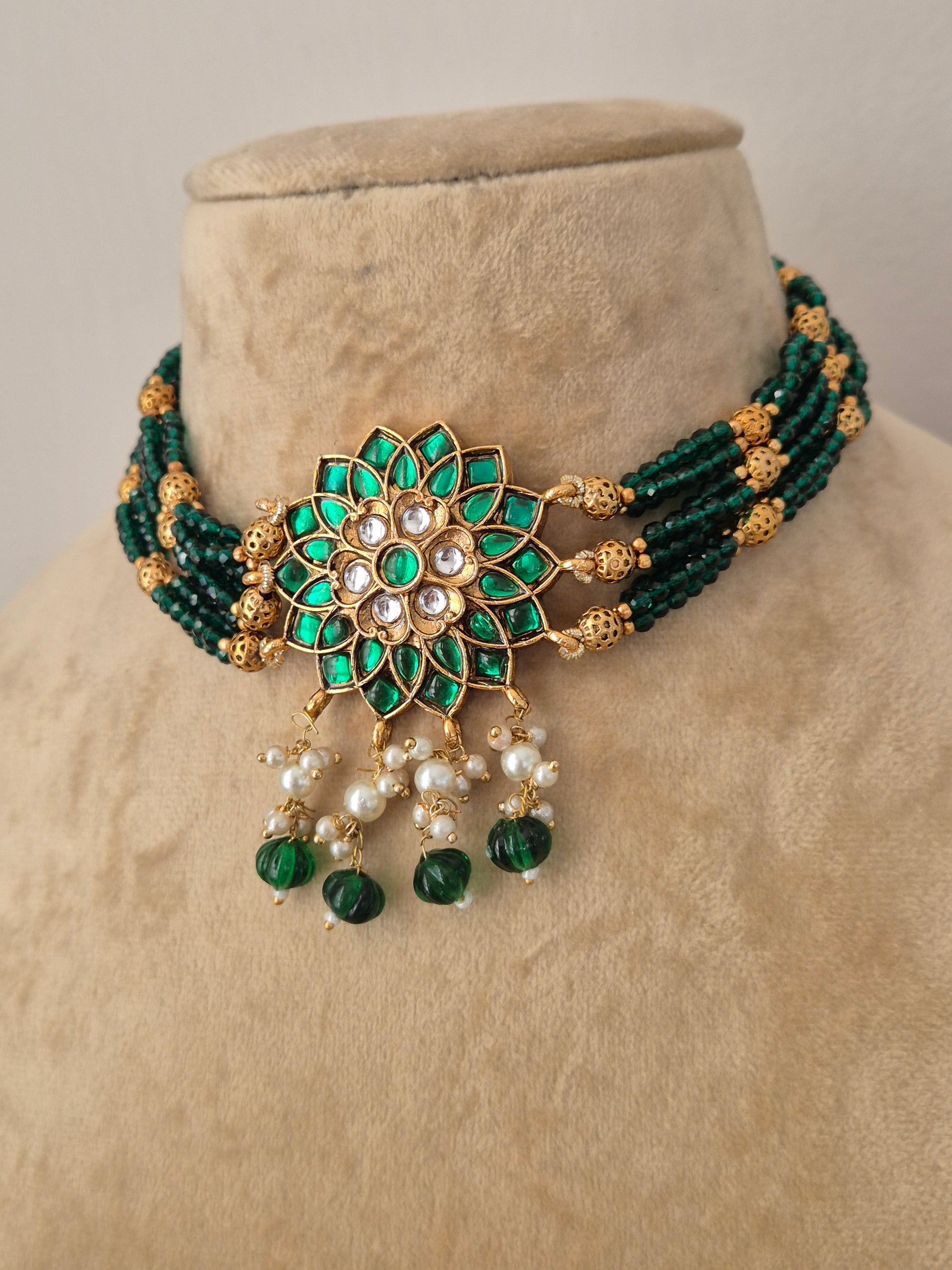 Indian ethnic jewelry set featuring a dark green beaded collar choker with a prominent gold flower pendant set with white crystals and emerald-green stones, complete with hanging pearls by naitri.in
