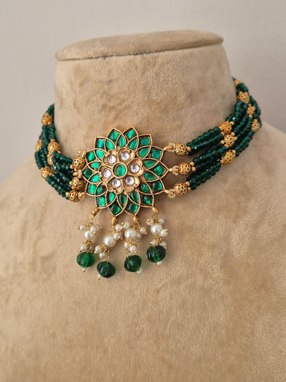 Indian ethnic jewelry set featuring a dark green beaded collar choker with a prominent gold flower pendant set with white crystals and emerald-green stones, complete with hanging pearls by naitri.in