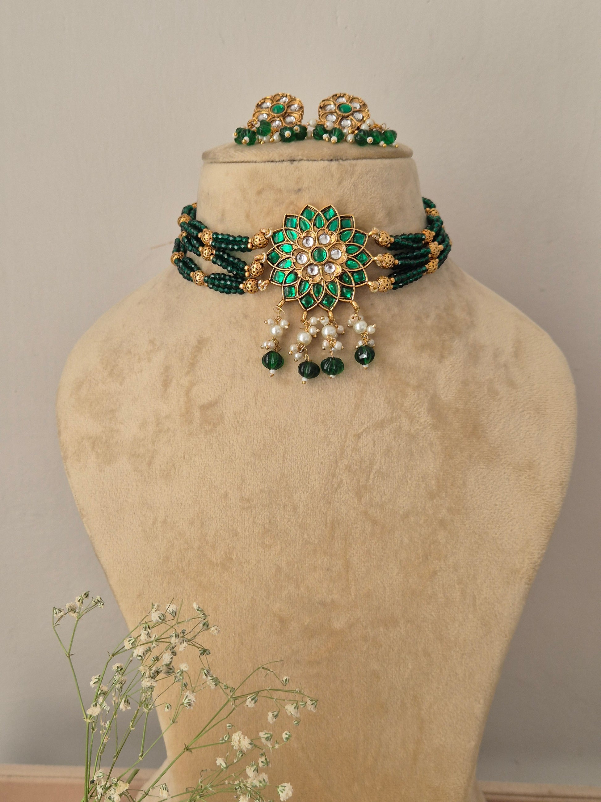 Traditional multi-strand green beaded choker necklace with a central gold floral pendant and matching earrings, by naitri.in