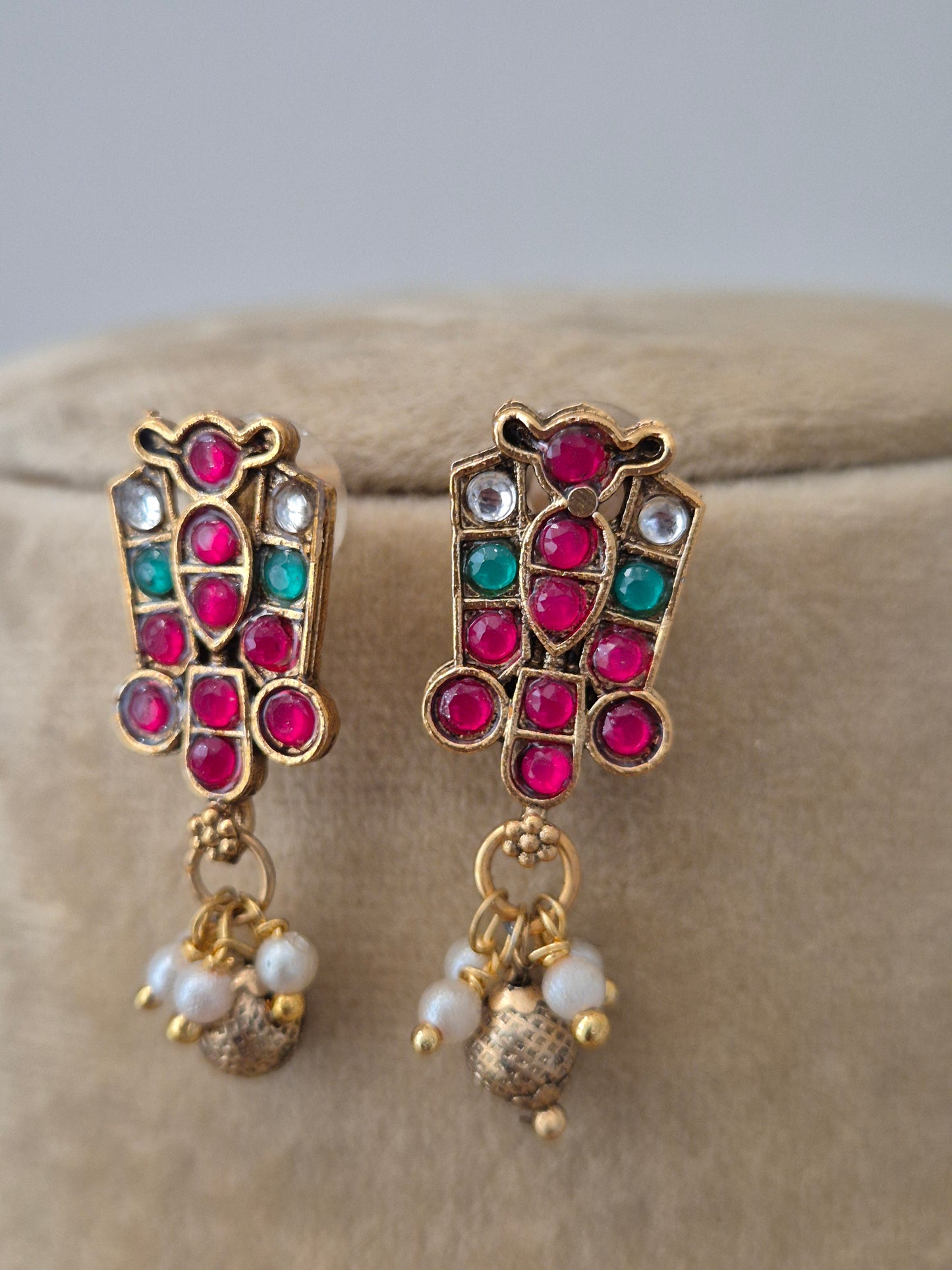 Golden ethnic earrings  by Naitri with intricate red and green stonework and matching hanging golg-pearls beads by naitri.in