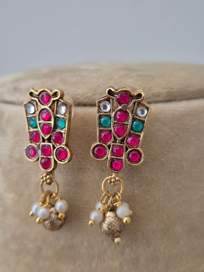 Golden ethnic earrings  by Naitri with intricate red and green stonework and matching hanging golg-pearls beads by naitri.in