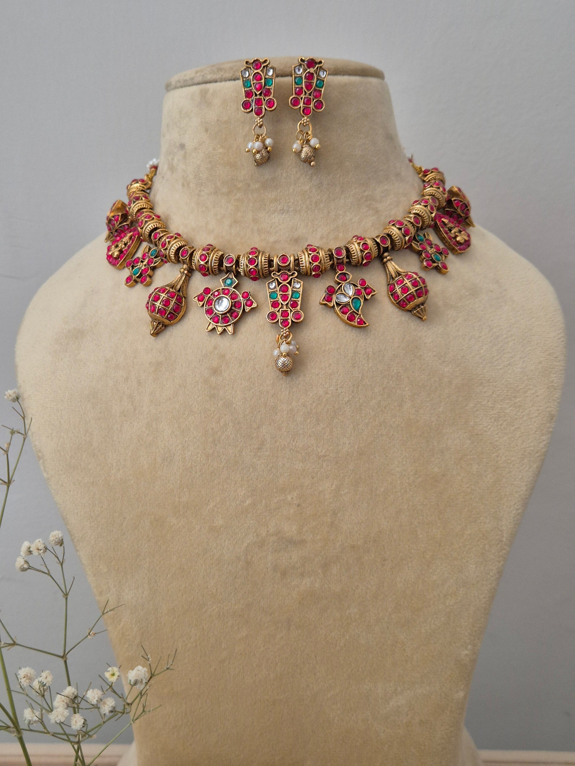 necklace set featuring an ornate matte gold choker with red and green stones, dangling kundan-style pendants, and matching drop earrings by naitri.in