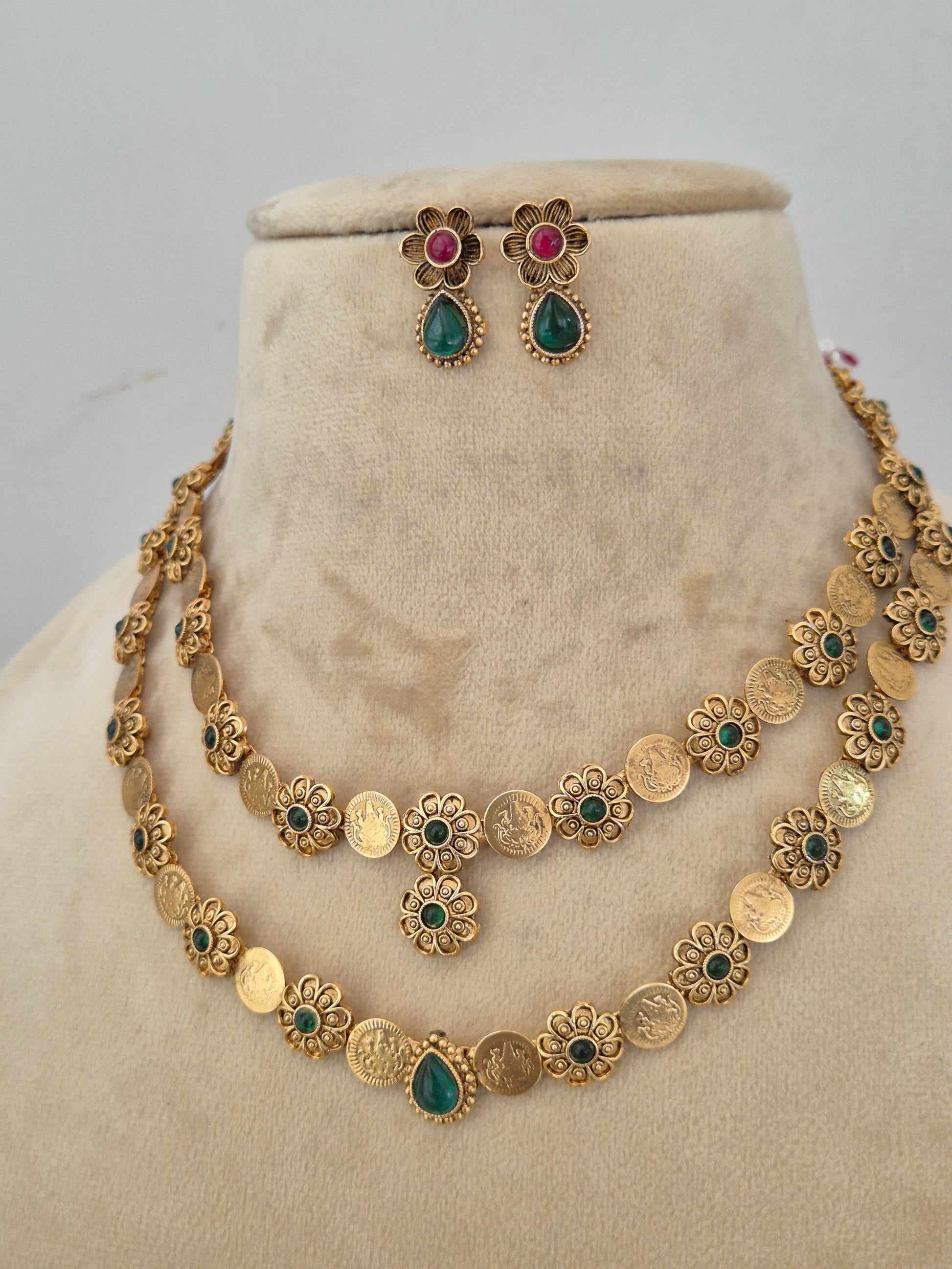 Gold-toned traditional jewelry set featuring a coin-patterned necklace with green and red stone accents and matching drop earrings by naitri.in