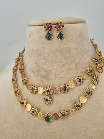 Gold-toned traditional jewelry set featuring a coin-patterned necklace with green and red stone accents and matching drop earrings by naitri.in